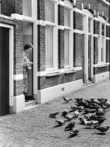 361136 Afbeelding van een vrouw die de duiven voert voor haar huis te Utrecht.